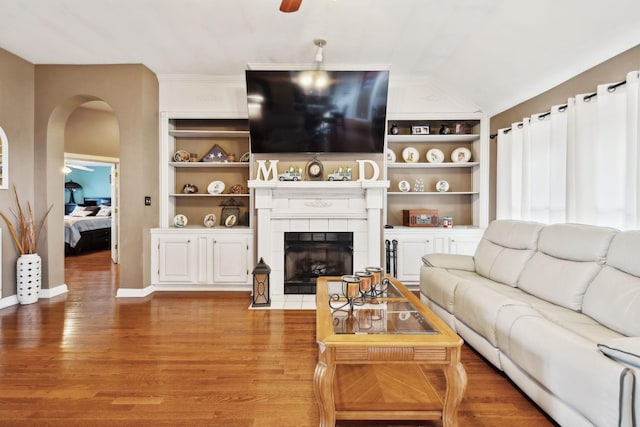 living room featuring ceiling fan, a fireplace, hardwood / wood-style floors, and built in features