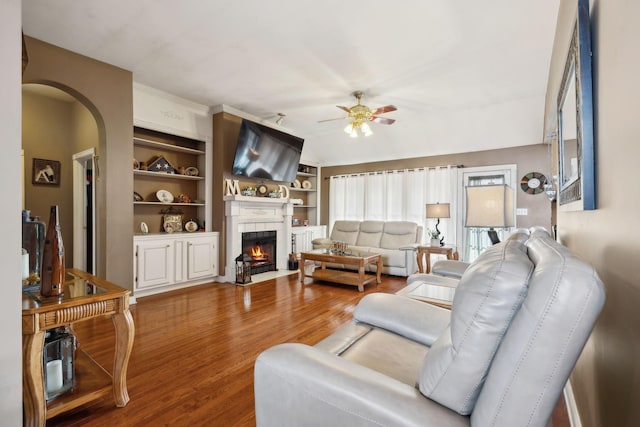 living room featuring hardwood / wood-style flooring, ceiling fan, a fireplace, and built in shelves