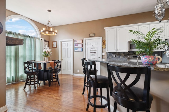 kitchen featuring pendant lighting, light hardwood / wood-style flooring, appliances with stainless steel finishes, white cabinetry, and dark stone counters