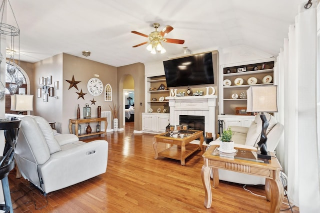 living room featuring a tiled fireplace, hardwood / wood-style floors, built in features, and ceiling fan