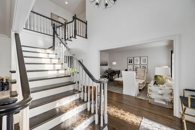 stairway with an inviting chandelier, hardwood / wood-style floors, crown molding, and a high ceiling