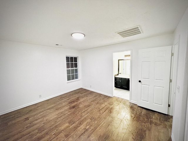 unfurnished bedroom with ensuite bath and dark wood-type flooring