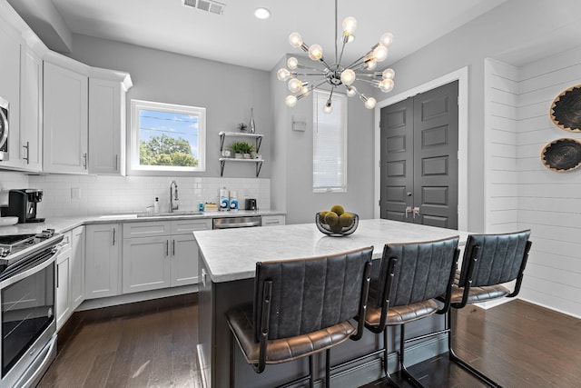 kitchen with sink, white cabinetry, stainless steel appliances, a kitchen island, and decorative light fixtures