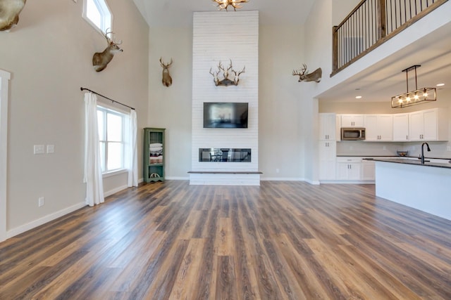 unfurnished living room with dark hardwood / wood-style floors, sink, a fireplace, and a towering ceiling