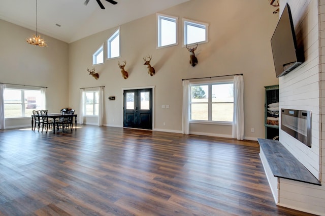 unfurnished living room with ceiling fan with notable chandelier, dark wood-type flooring, a large fireplace, and a towering ceiling