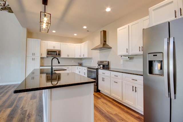 kitchen featuring a kitchen island with sink, stainless steel appliances, white cabinets, wall chimney exhaust hood, and light wood-type flooring