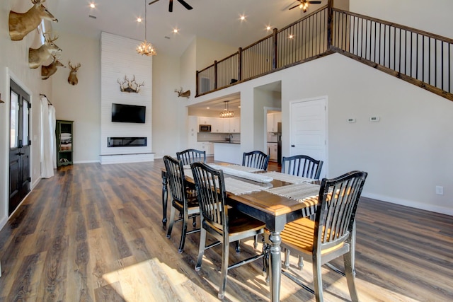 dining area with an inviting chandelier, a towering ceiling, wood-type flooring, and a large fireplace