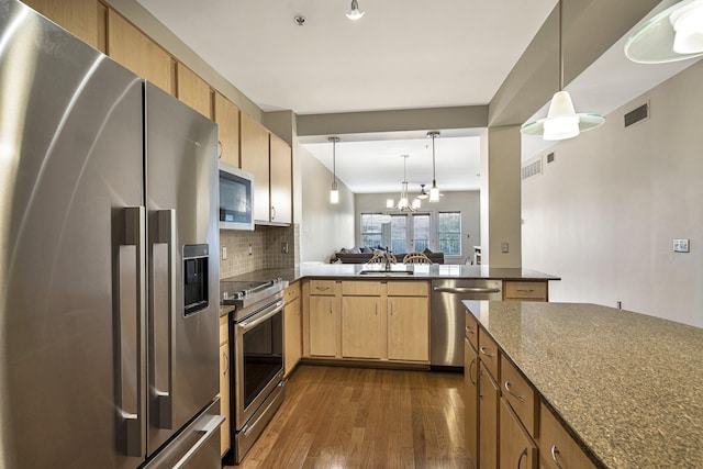 kitchen with backsplash, hanging light fixtures, kitchen peninsula, stainless steel appliances, and dark wood-type flooring