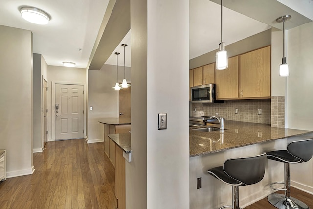 kitchen featuring dark stone counters, kitchen peninsula, sink, and hanging light fixtures