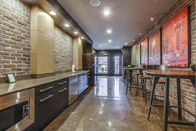 kitchen featuring stainless steel microwave, sink, a breakfast bar area, and dark stone countertops