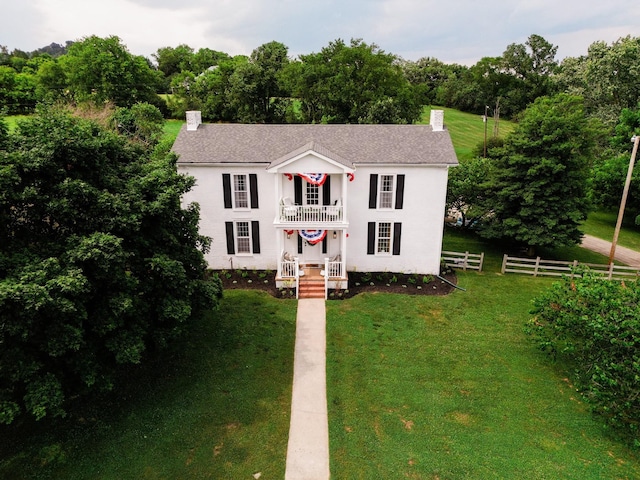 colonial home featuring a balcony and a front lawn