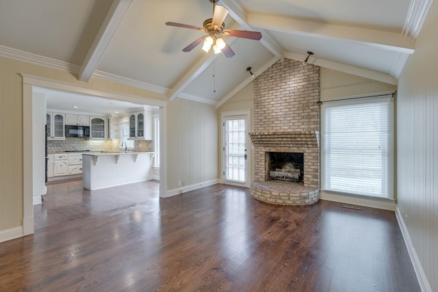 unfurnished living room with sink, ceiling fan, a fireplace, lofted ceiling with beams, and dark hardwood / wood-style flooring