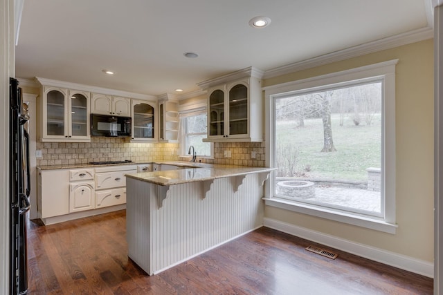 kitchen with a breakfast bar area, white cabinetry, light stone countertops, decorative backsplash, and black appliances