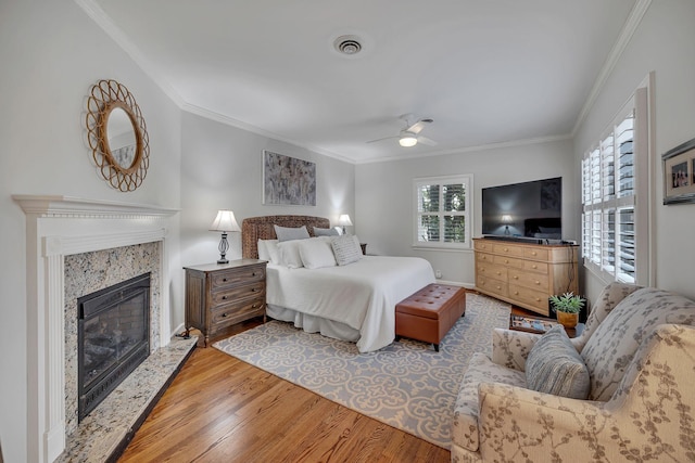 bedroom featuring crown molding, ceiling fan, a premium fireplace, and light hardwood / wood-style flooring