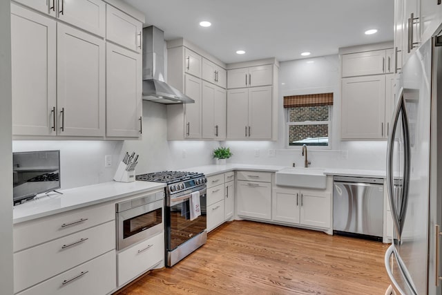 kitchen featuring wall chimney exhaust hood, sink, white cabinetry, light wood-type flooring, and stainless steel appliances