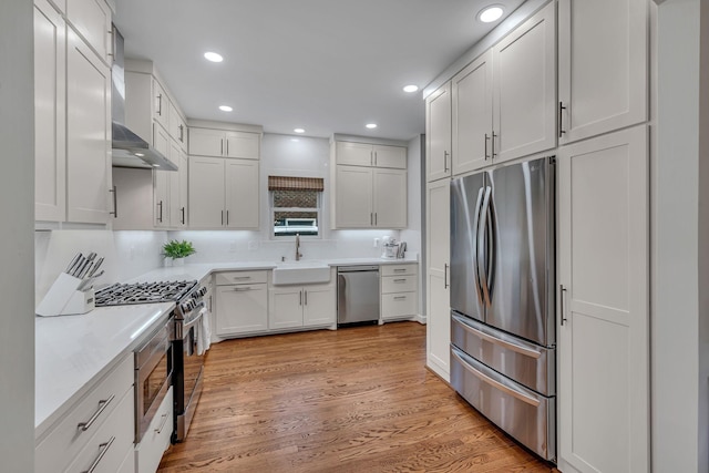 kitchen with wall chimney exhaust hood, sink, stainless steel appliances, light hardwood / wood-style floors, and white cabinets