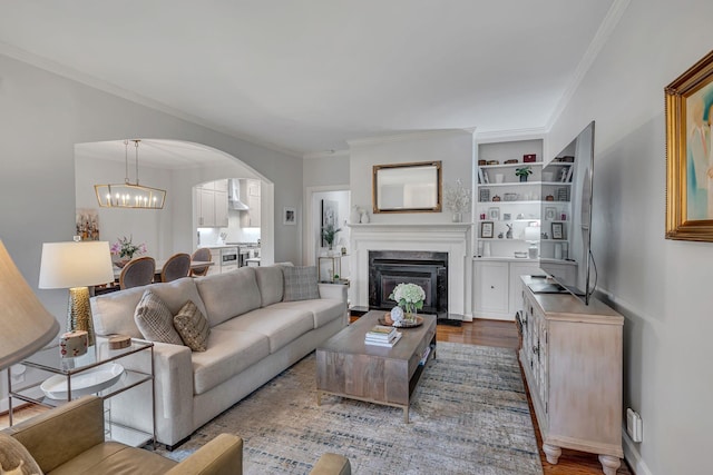 living room with built in features, hardwood / wood-style flooring, a high end fireplace, crown molding, and an inviting chandelier