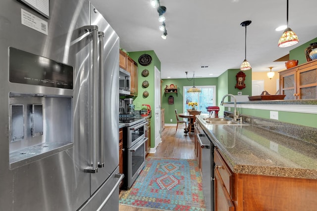 kitchen featuring stone countertops, decorative light fixtures, sink, stainless steel appliances, and light hardwood / wood-style flooring