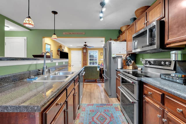 kitchen with sink, appliances with stainless steel finishes, a kitchen island, pendant lighting, and light hardwood / wood-style floors