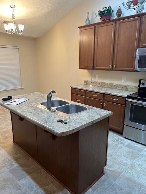 kitchen with sink, an island with sink, a textured ceiling, and appliances with stainless steel finishes