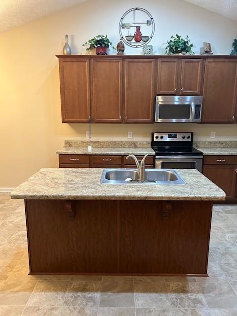 kitchen featuring lofted ceiling, sink, stainless steel appliances, and an island with sink