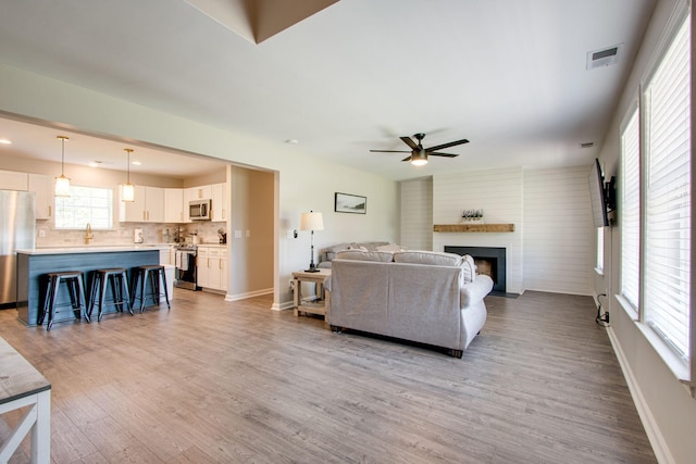 living room featuring ceiling fan, a large fireplace, and light hardwood / wood-style floors