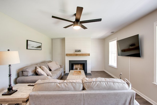 living room featuring ceiling fan, a large fireplace, and dark hardwood / wood-style flooring