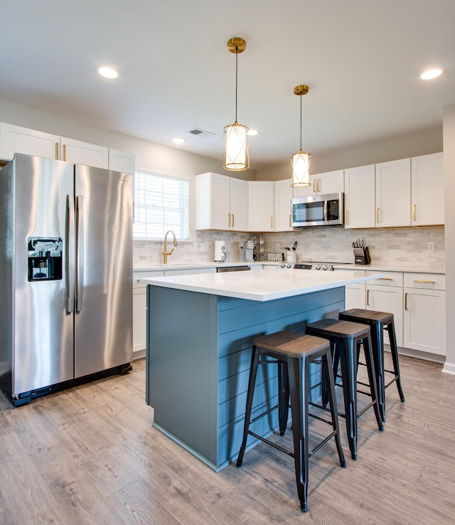 kitchen with appliances with stainless steel finishes, pendant lighting, white cabinets, and light hardwood / wood-style floors