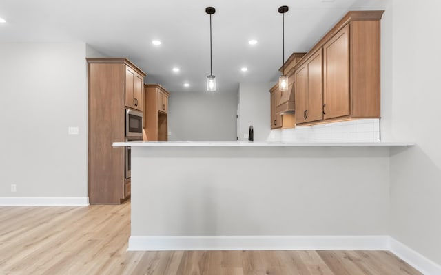 kitchen with built in microwave, backsplash, light hardwood / wood-style floors, and decorative light fixtures