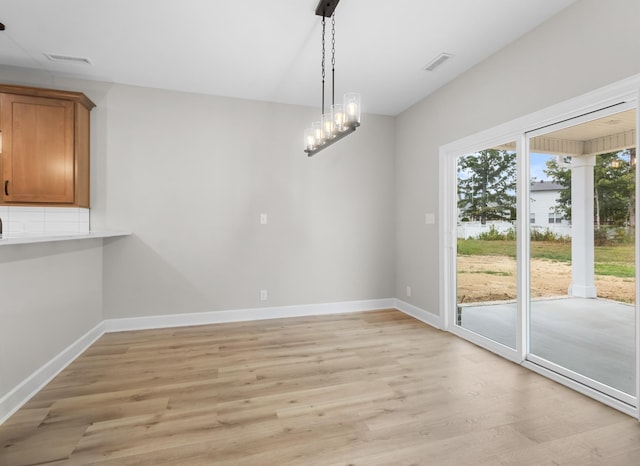 unfurnished dining area with an inviting chandelier and light hardwood / wood-style flooring