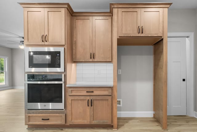 kitchen featuring built in microwave, decorative backsplash, stainless steel oven, ceiling fan, and light wood-type flooring