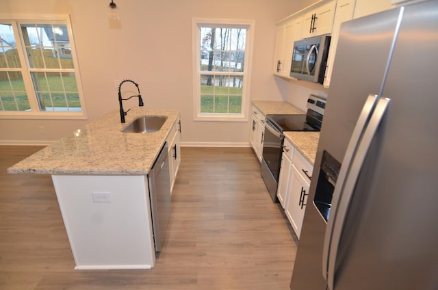 kitchen featuring sink, a center island with sink, appliances with stainless steel finishes, light stone countertops, and white cabinets