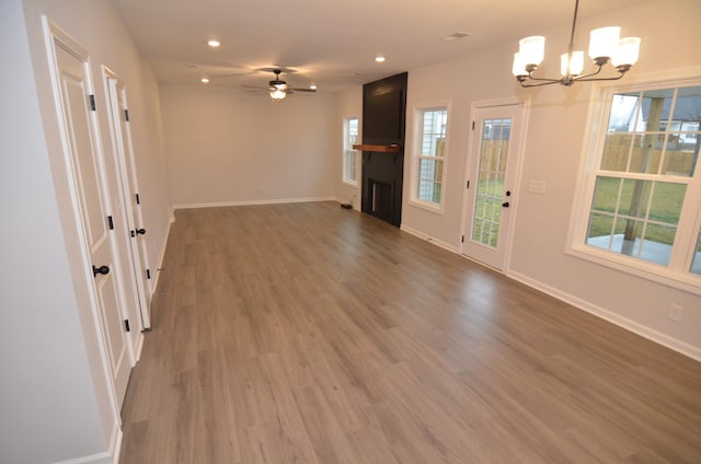 unfurnished living room featuring hardwood / wood-style flooring, a fireplace, and ceiling fan with notable chandelier