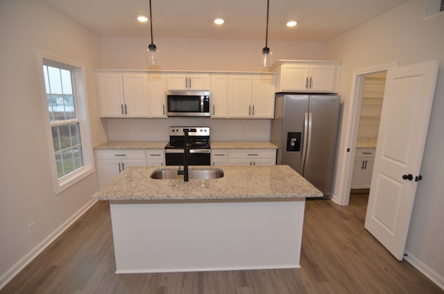 kitchen with white cabinetry, hanging light fixtures, appliances with stainless steel finishes, an island with sink, and light stone countertops