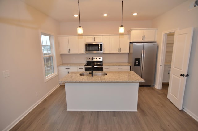 kitchen with a center island with sink, appliances with stainless steel finishes, pendant lighting, light stone countertops, and white cabinets