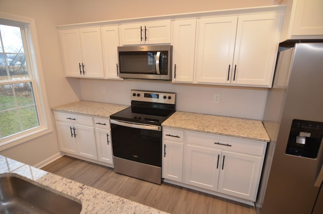 kitchen featuring sink, white cabinetry, stainless steel appliances, light stone countertops, and light hardwood / wood-style floors