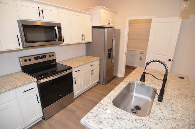 kitchen with sink, light stone counters, light wood-type flooring, stainless steel appliances, and white cabinets