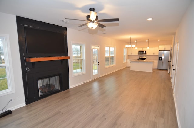 unfurnished living room with ceiling fan with notable chandelier, a fireplace, and light hardwood / wood-style floors