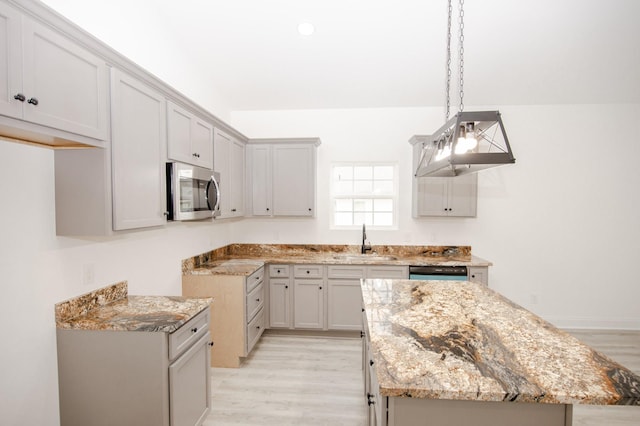 kitchen with gray cabinets, decorative light fixtures, sink, stainless steel appliances, and light hardwood / wood-style flooring