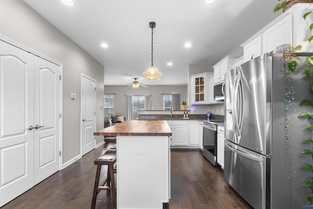 kitchen featuring wood counters, a kitchen bar, white cabinetry, appliances with stainless steel finishes, and a kitchen island