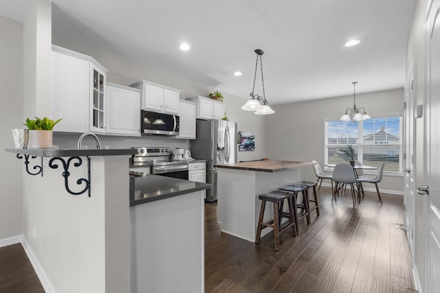 kitchen featuring white cabinetry, stainless steel appliances, a kitchen bar, decorative light fixtures, and kitchen peninsula