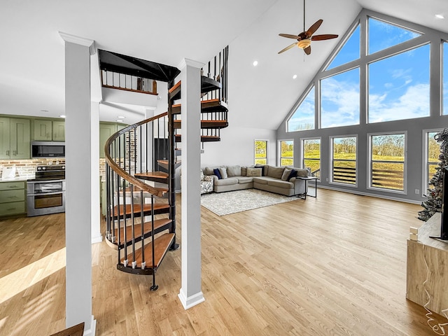 living area with a ceiling fan, stairway, a towering ceiling, and light wood-style floors