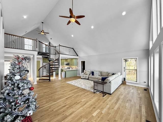 living room featuring stairway, baseboards, light wood-style flooring, and a high ceiling