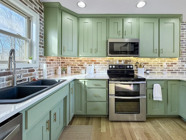 kitchen featuring appliances with stainless steel finishes, light countertops, a sink, and green cabinets