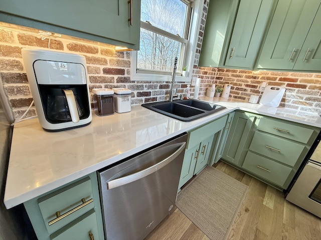 kitchen featuring brick wall, stainless steel dishwasher, light wood-style floors, green cabinets, and a sink