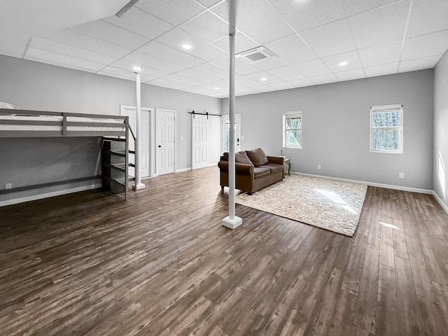 interior space featuring a barn door, baseboards, visible vents, a drop ceiling, and dark wood-style flooring