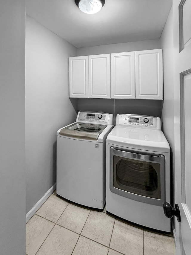 laundry area with light tile patterned flooring, washing machine and clothes dryer, cabinet space, and baseboards