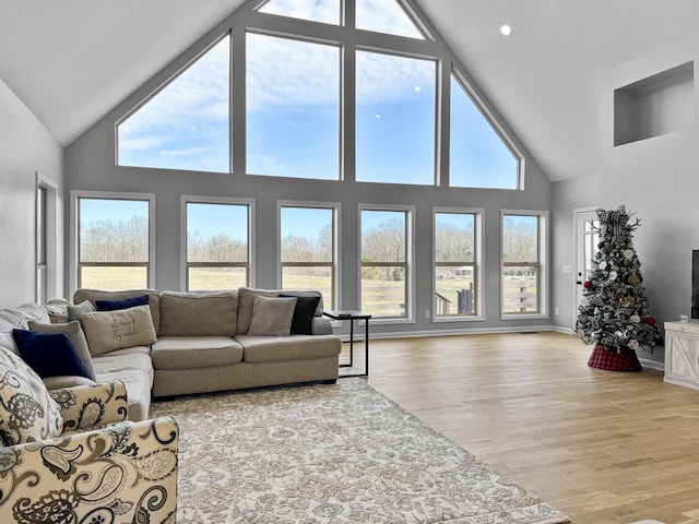 living area featuring light wood-style floors, high vaulted ceiling, and baseboards