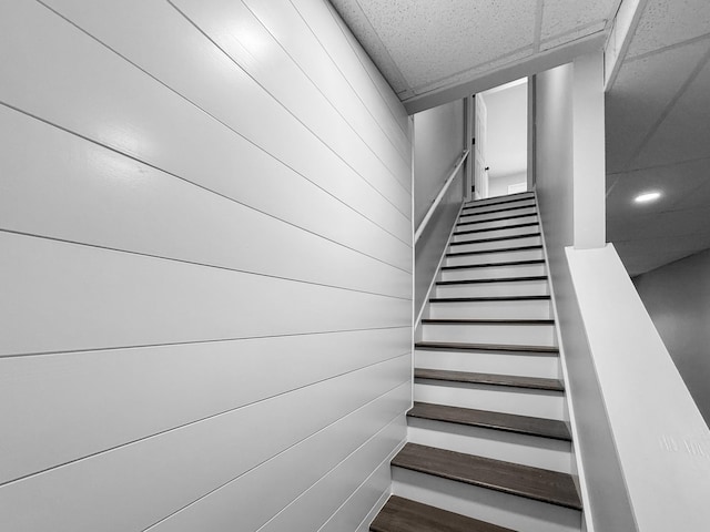 stairway with a paneled ceiling and wood walls