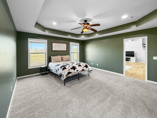 carpeted bedroom with a ceiling fan, a raised ceiling, and baseboards